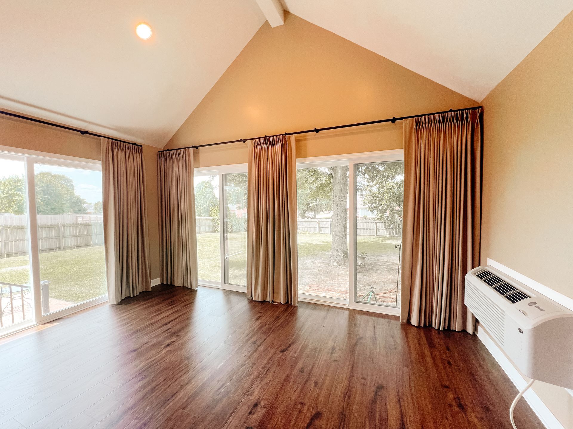 An empty living room with hardwood floors and sliding glass doors with custom drapes.