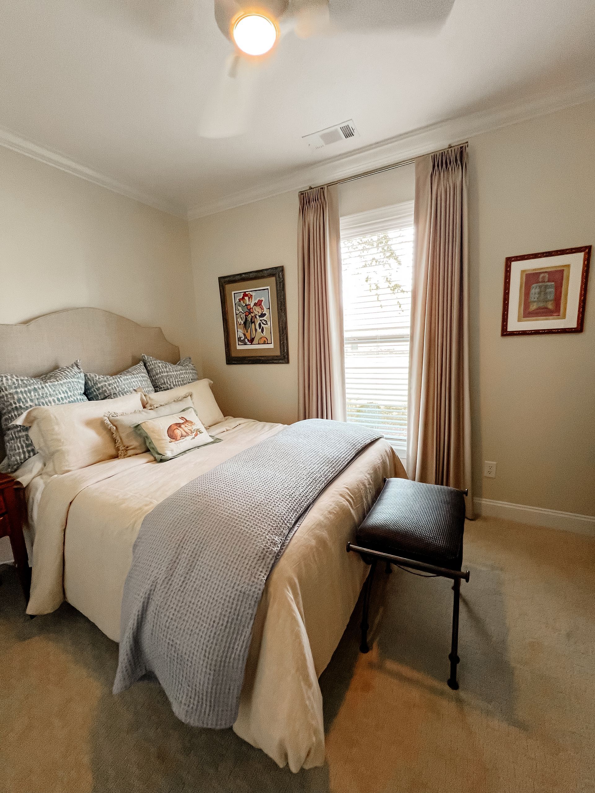 A bedroom with a large bed and a ceiling fan and custom drapes on the windows.