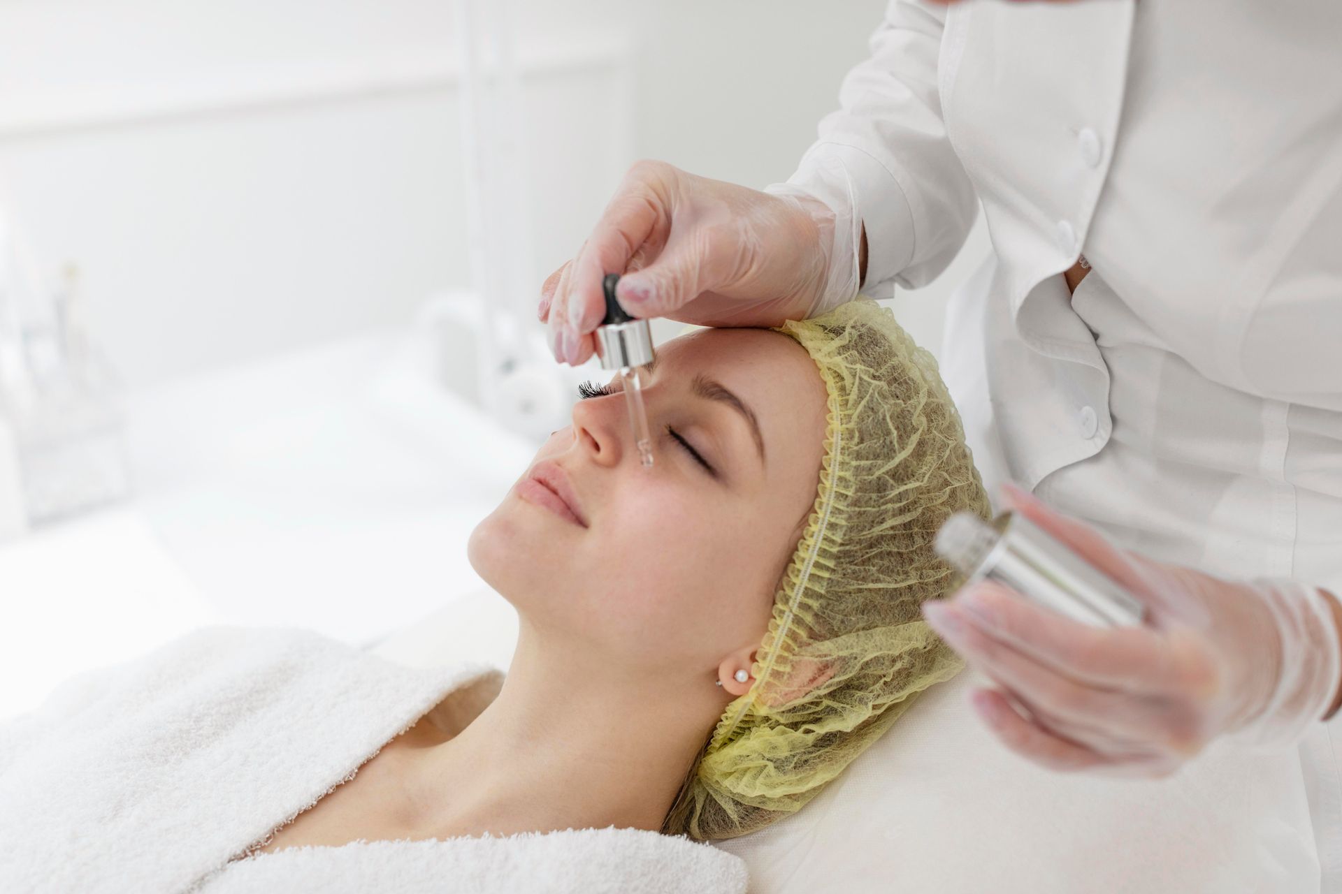 Woman receiving facial serum from a dropper in a bright spa setting.