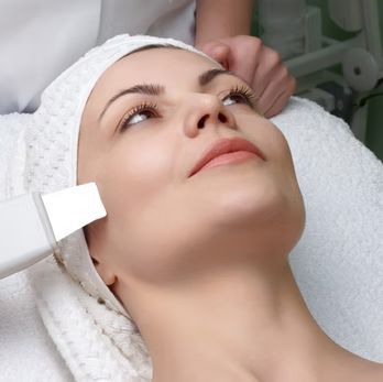 Woman receiving facial treatment with an ultrasonic skin spatula at a spa.