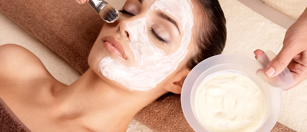 Woman receiving facial treatment with cream mask in a spa.
