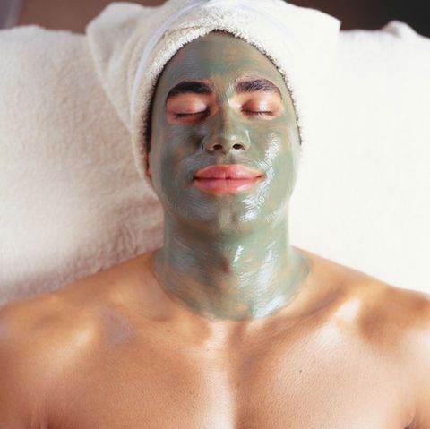 Man with face mask and towel on head, relaxing on white surface.