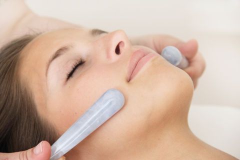 Woman receiving facial massage with cool, light-colored jade tools.