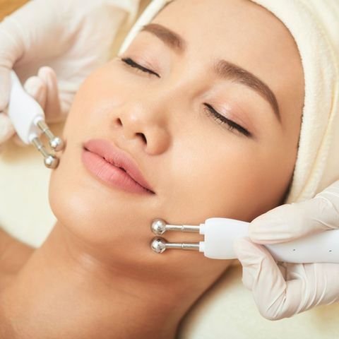 Woman receiving facial treatment with metal wands, eyes closed, hands gloved.