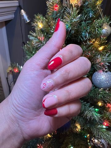 Hand with red and white Christmas-themed nail art in front of a decorated Christmas tree.