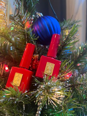 Two red nail polish bottles on a Christmas tree, with a blue ornament and lights.