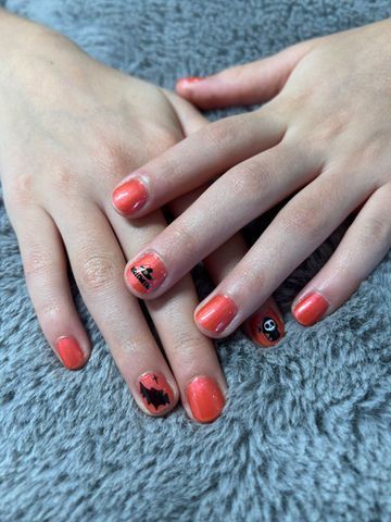 Hands with coral nail polish, some with black decorative designs, resting on a gray textured surface.