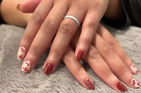Hands with red glitter and white nails with red designs.