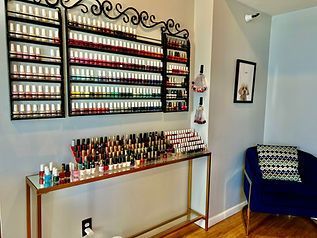 Nail polish display in a salon. Many colorful bottles on shelves, a table, and a chair.