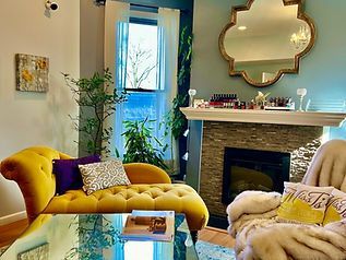 Cozy living room with yellow chaise lounge, fireplace, mirror, and plants.