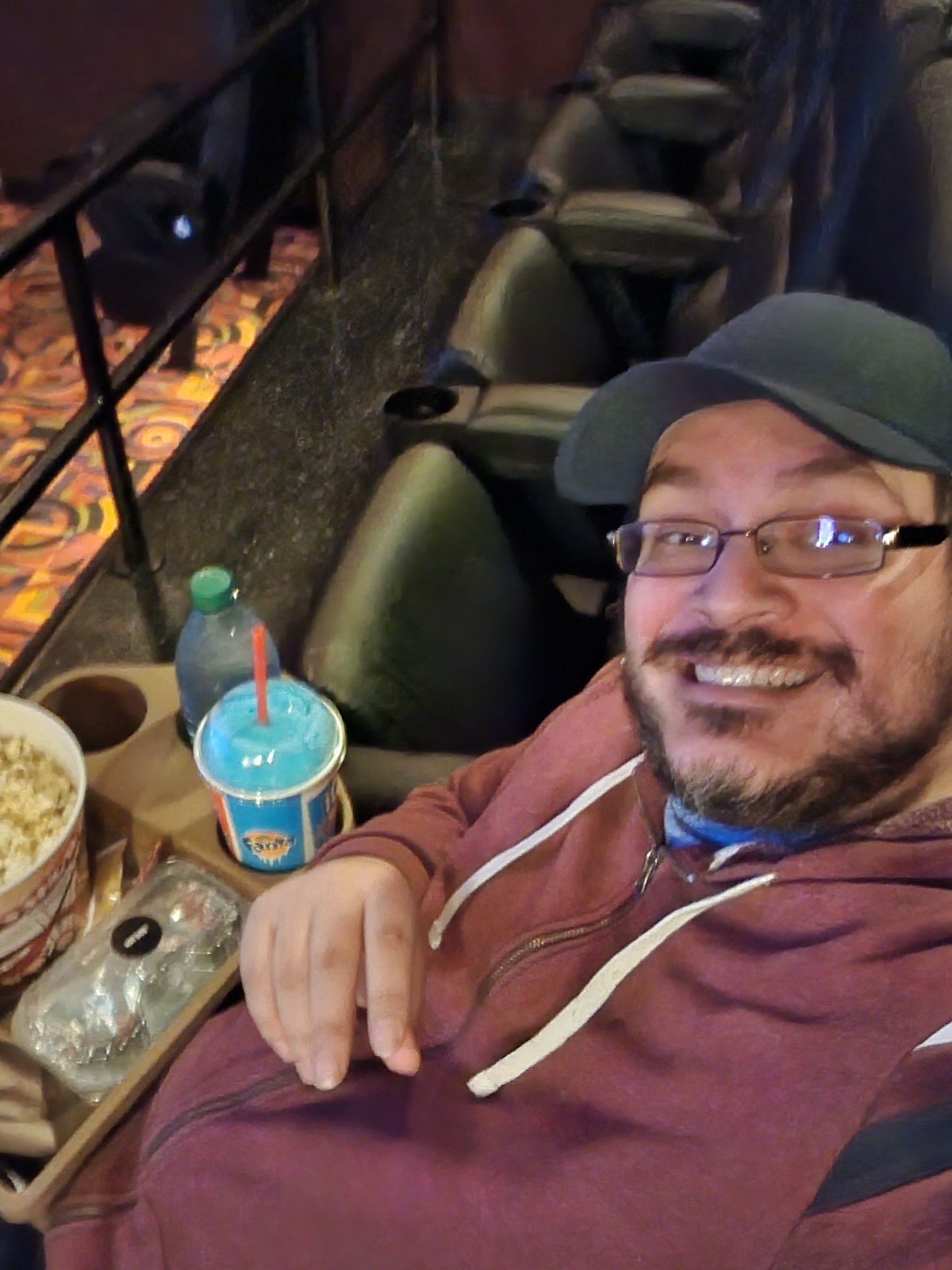A man wearing glasses and a hat is sitting in a movie theater