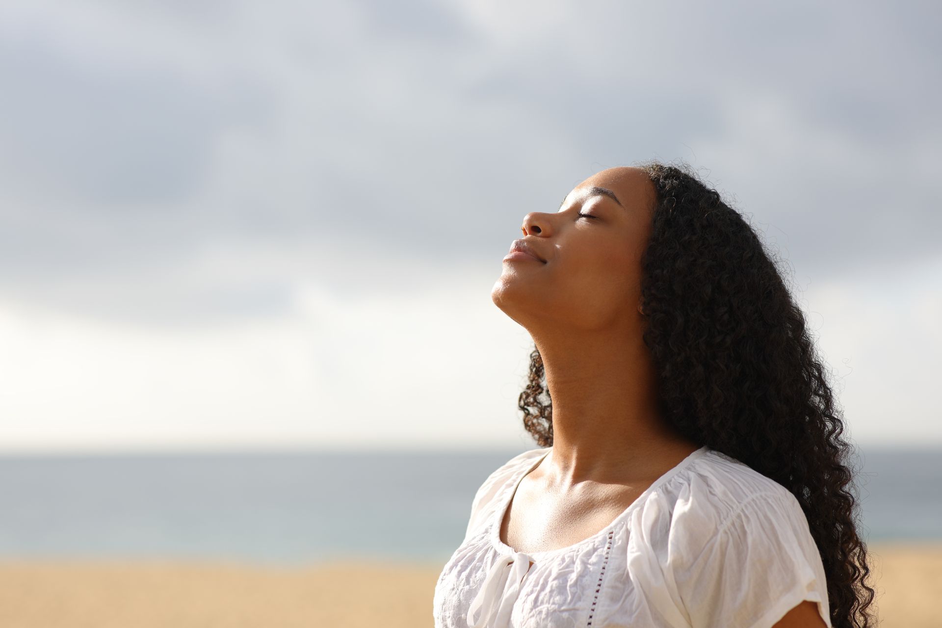 Woman with closed eyes enjoying the sun at the beach, looking up.