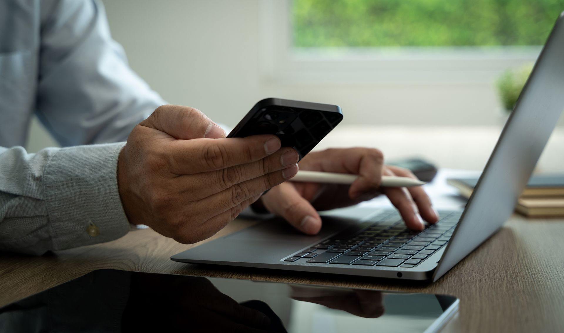 Person using a laptop and a smartphone at a desk.