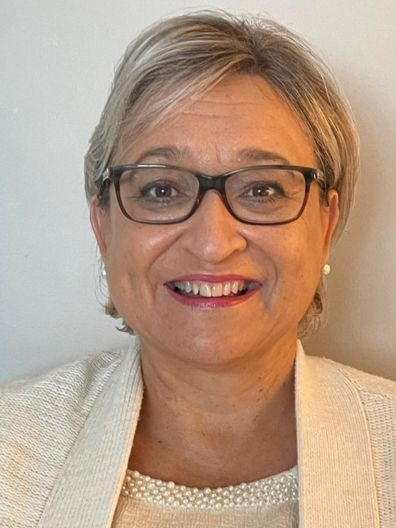 A woman wearing glasses and a white jacket is smiling for the camera.