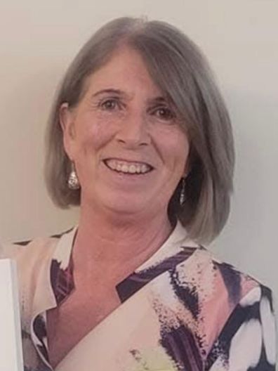 A woman with gray hair is smiling and holding a piece of paper.