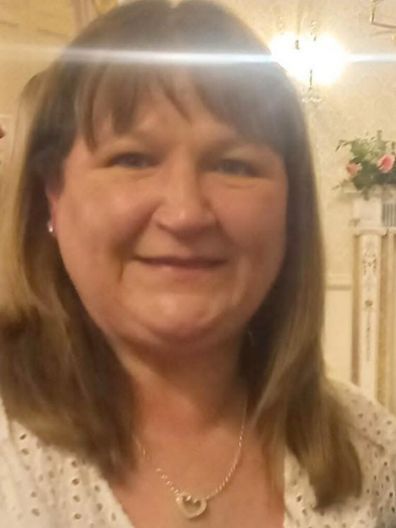 A woman wearing a heart shaped necklace is smiling for the camera.