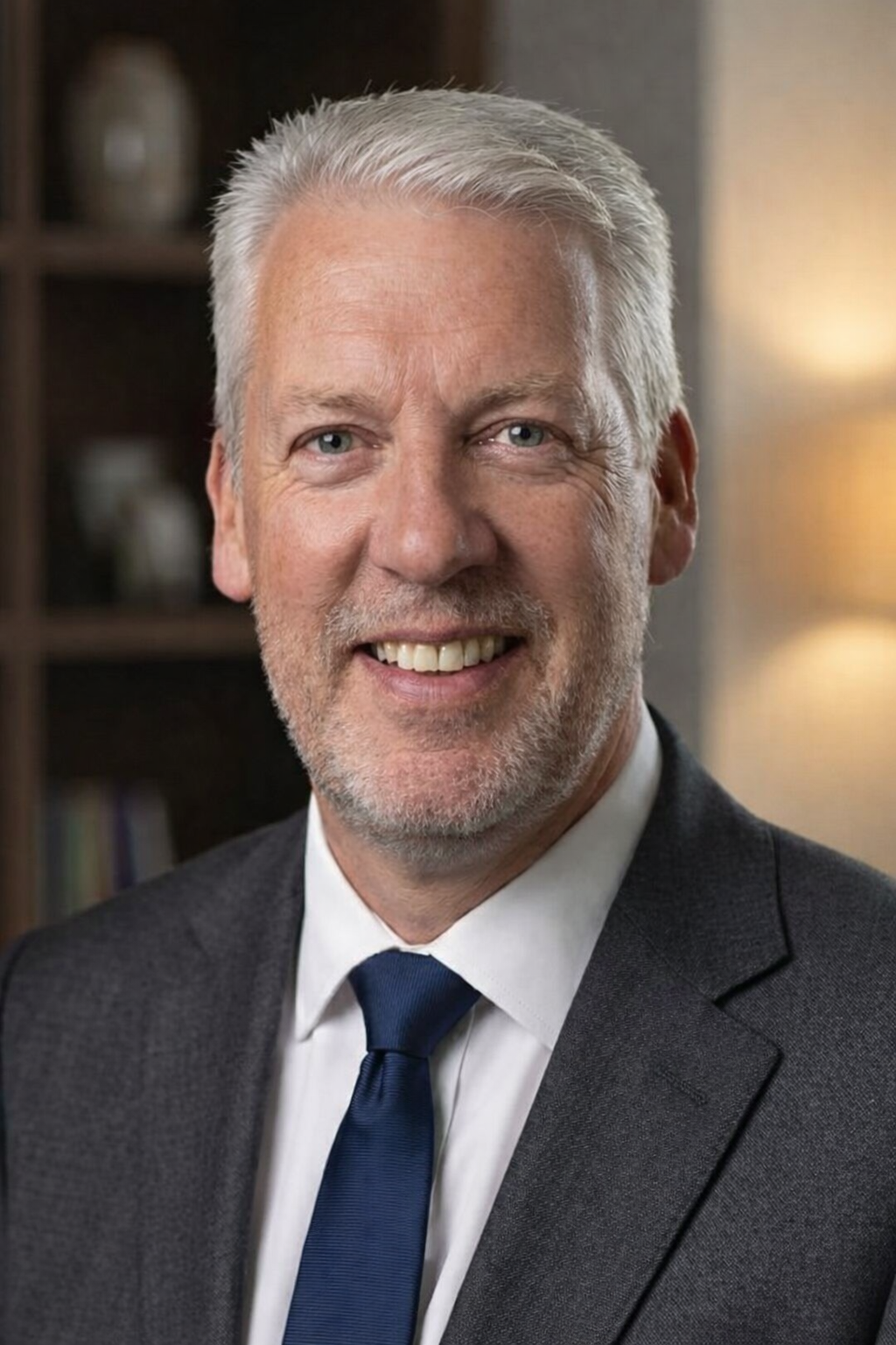 Man with gray hair smiling, wearing a light blue striped button-down shirt.