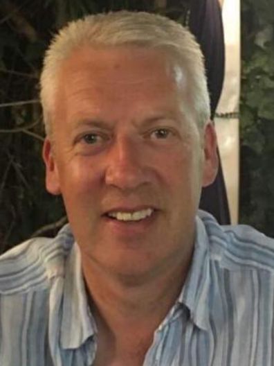 Man with gray hair smiling, wearing a light blue striped button-down shirt.