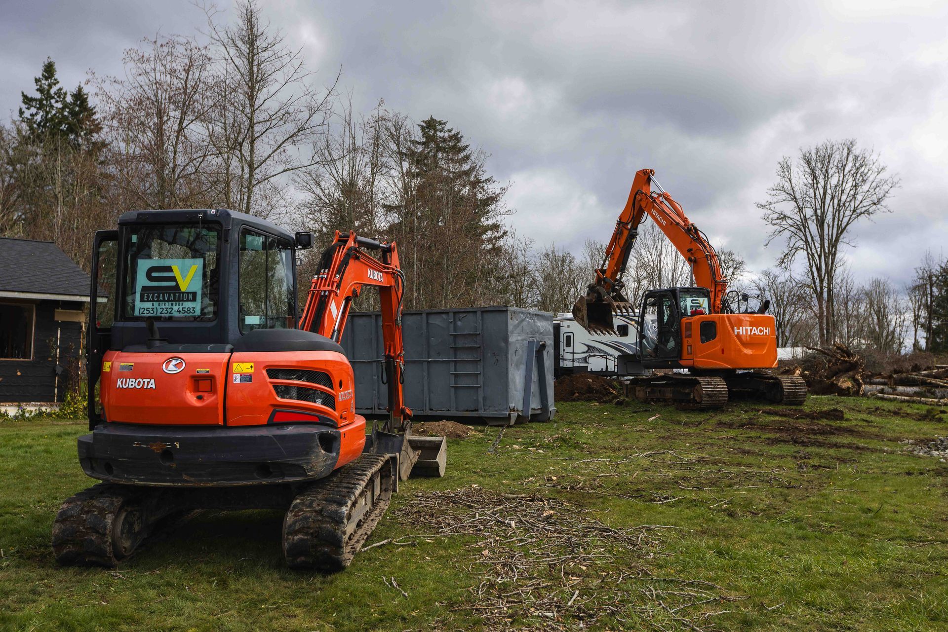 A small orange excavator is parked in a grassy field next to a large orange excavator.