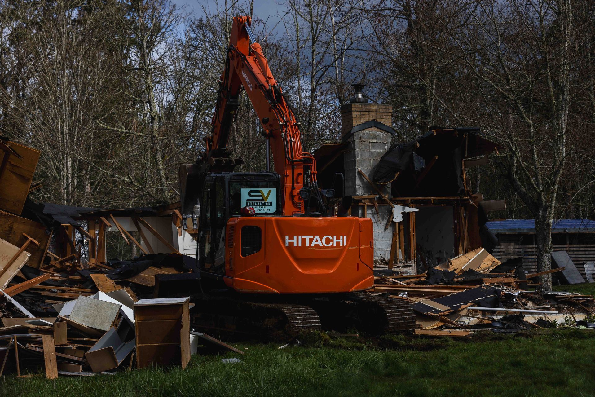A hitachi excavator is demolishing a house in a field