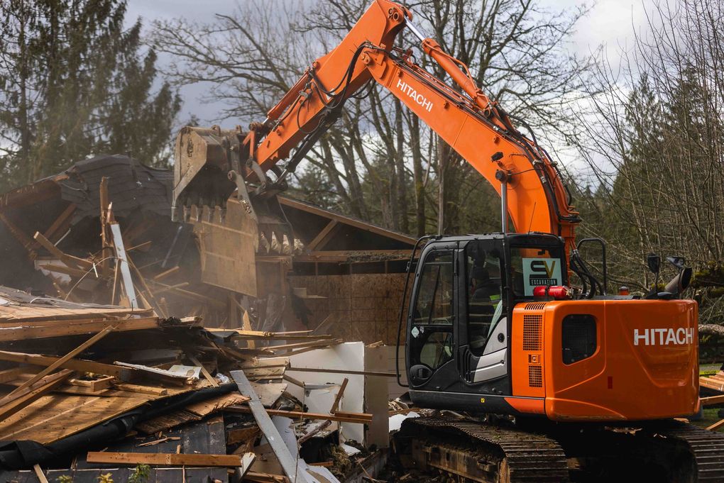 A large orange excavator is demolishing a house.