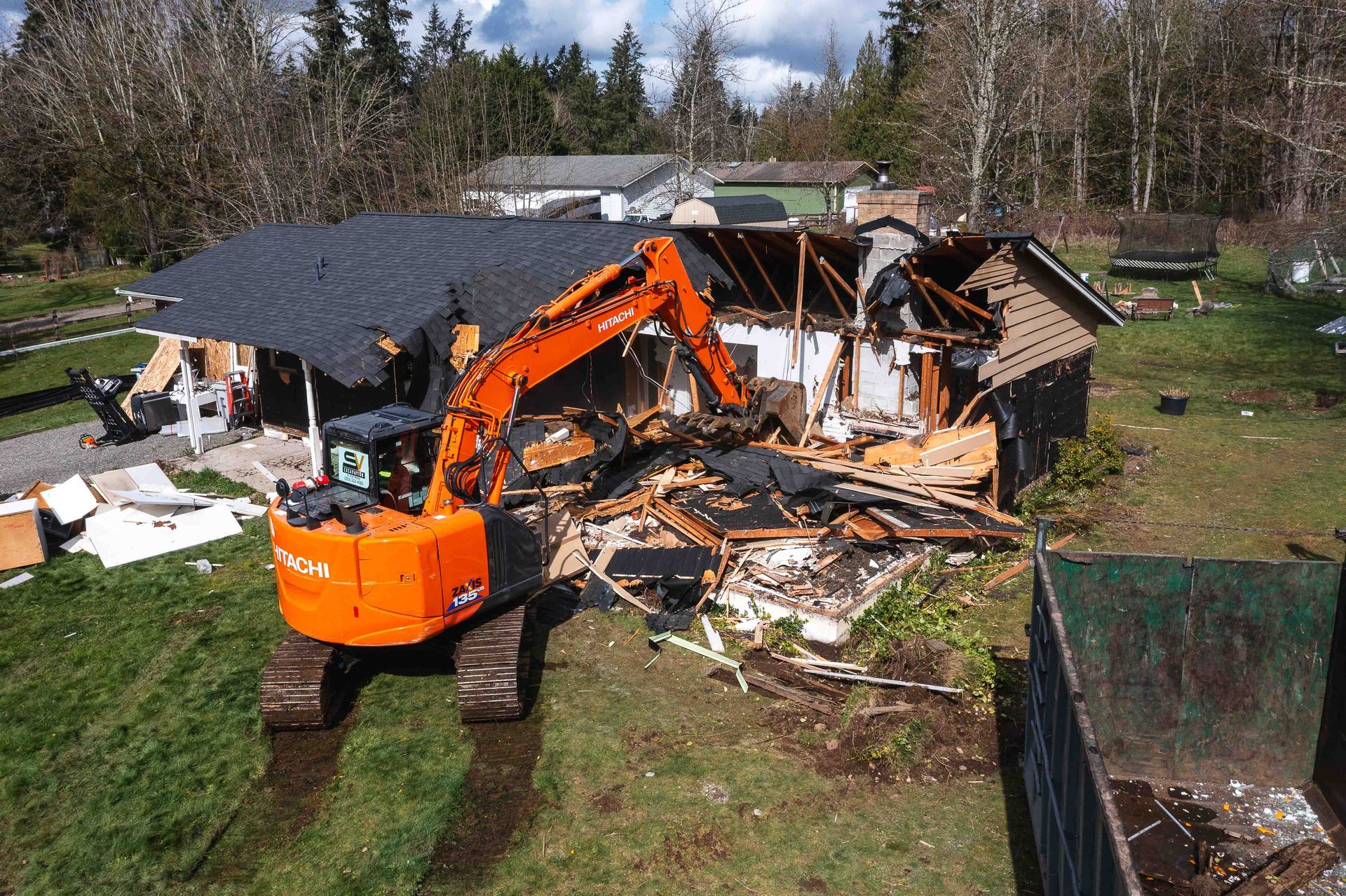 An aerial view of a house being demolished by an excavator.