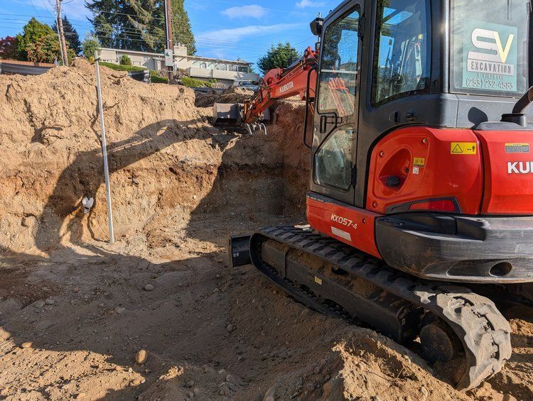 A red and black excavator is digging a hole in the dirt.