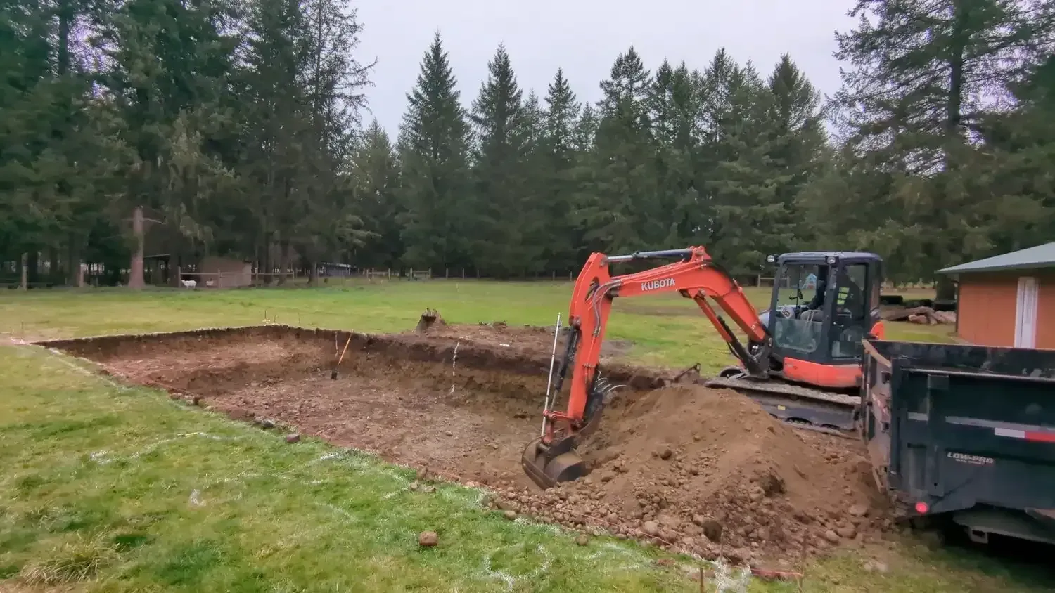 An excavator is digging a hole in the ground in a yard.