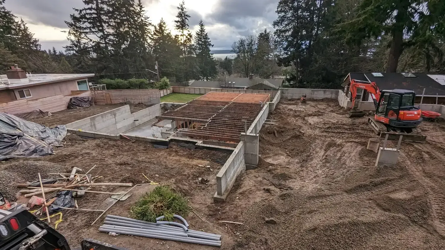 A construction site with a house in the background and an excavator in the foreground.