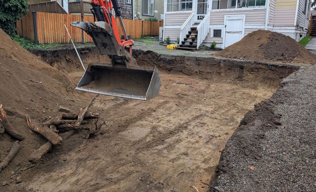 A bulldozer is digging a hole in the dirt in front of a house.
