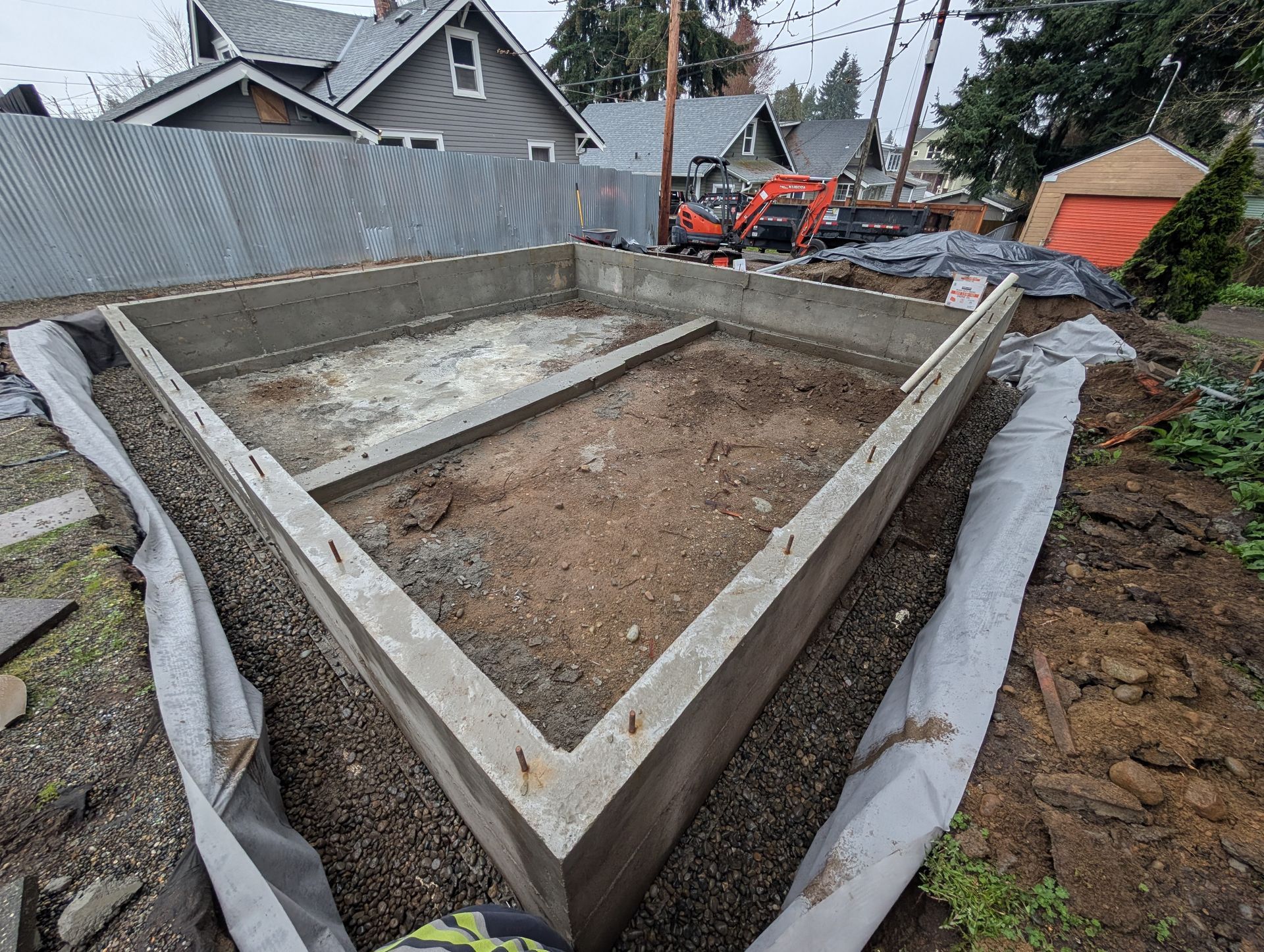 A concrete foundation is being built in the backyard of a house.