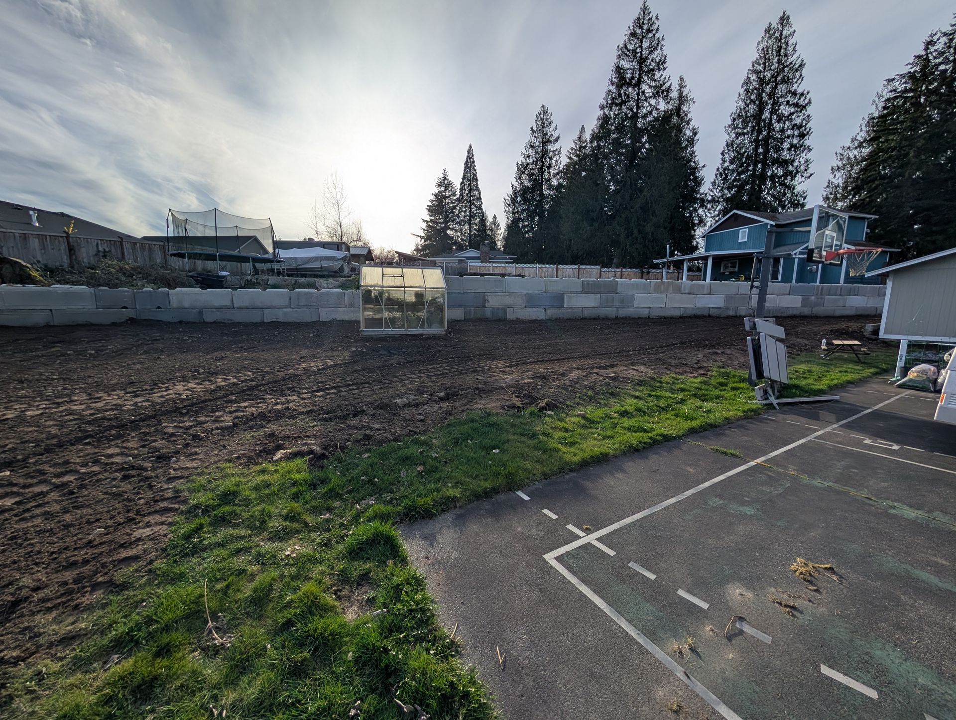 A fenced in yard with a greenhouse and a house in the background
