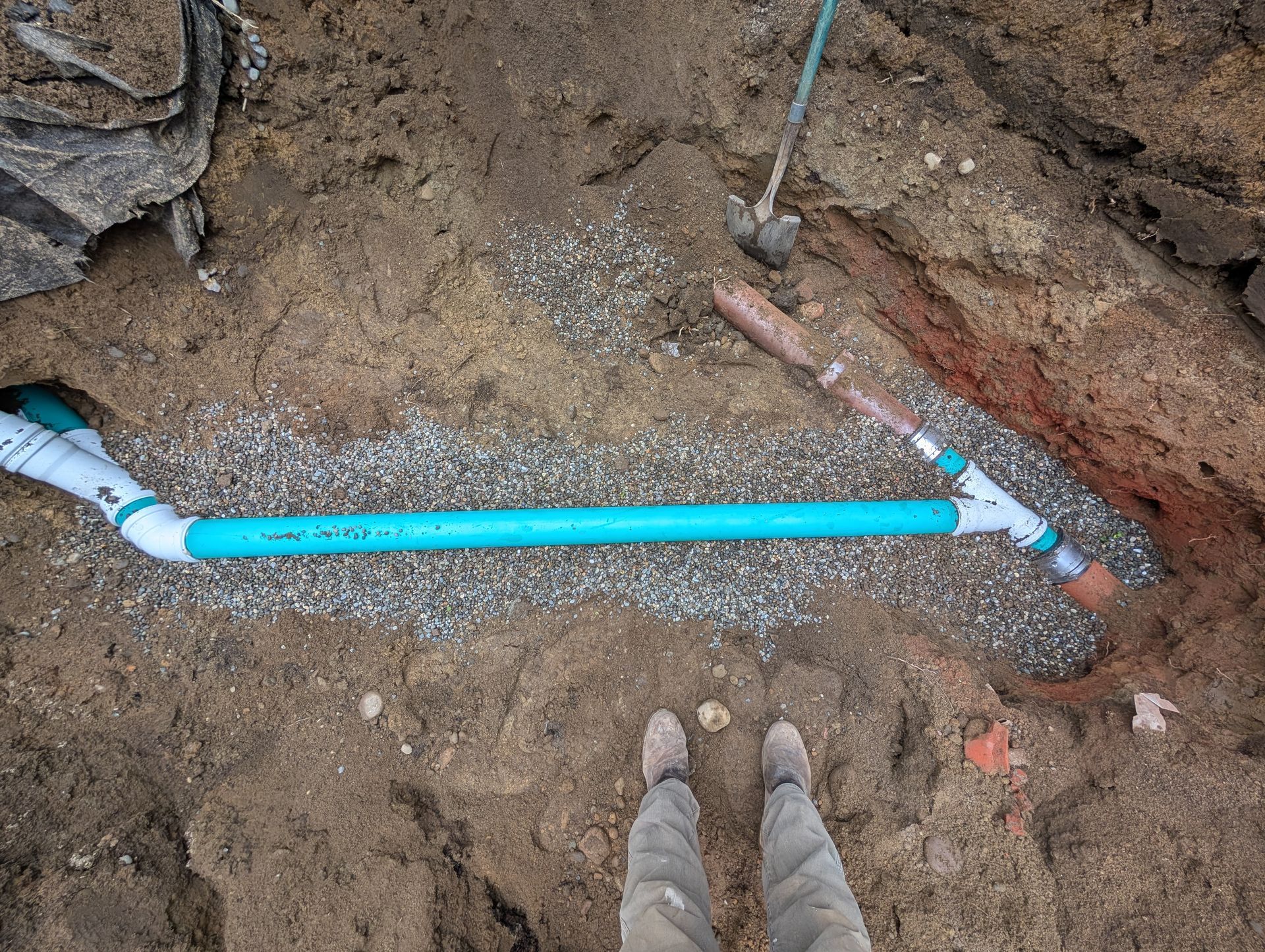 A person is standing next to a blue pipe in the dirt.