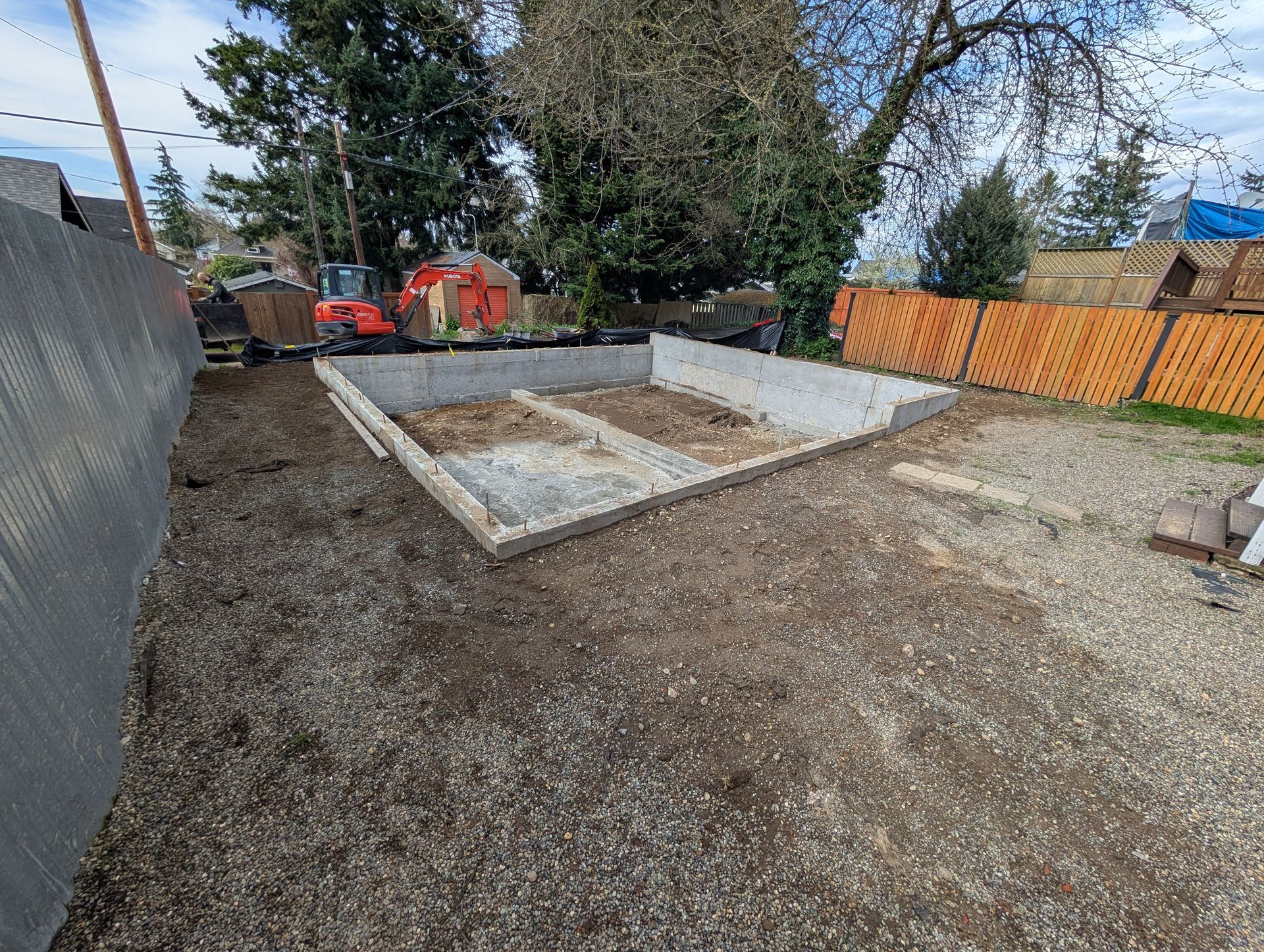 A concrete foundation is being built in the backyard of a house.