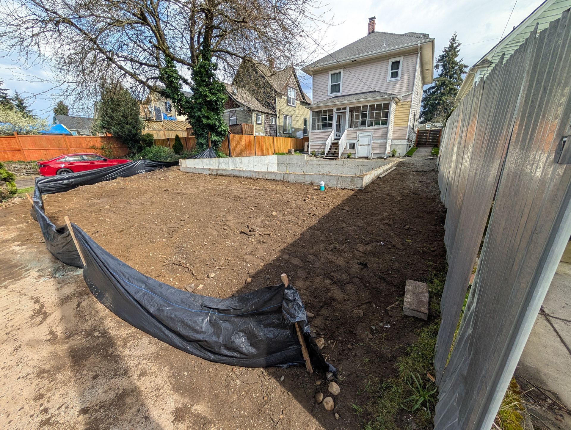 A fence is surrounding a dirt field in front of a house.