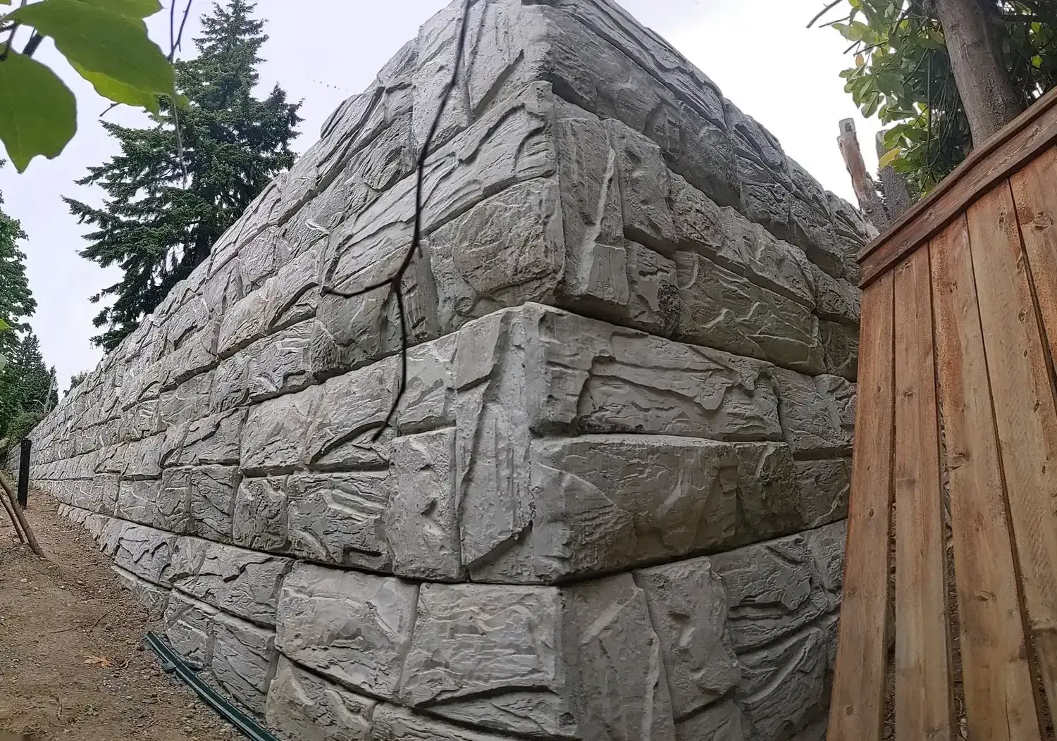 A large stone wall with a wooden fence in the background.