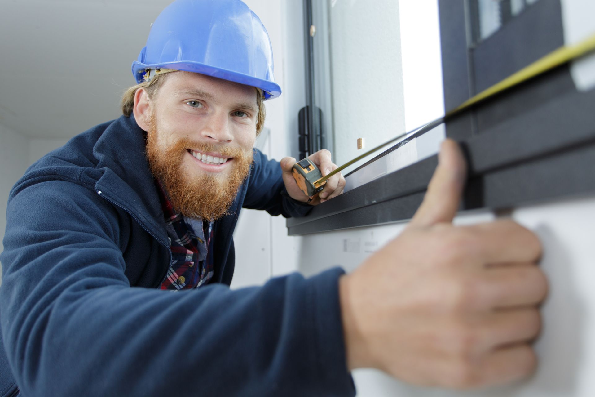 A man is measuring a window with a tape measure and giving a thumbs up.