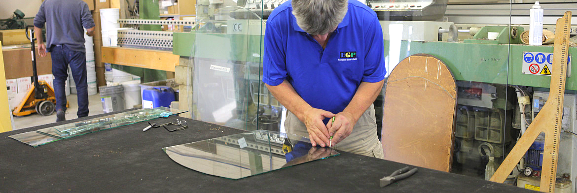 A man is cutting a piece of glass on a table in a factory.