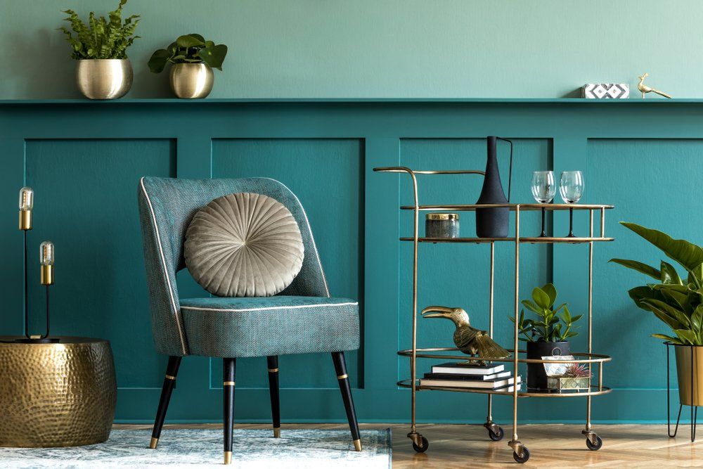 A living room with green walls , a chair , a table and a bar cart.