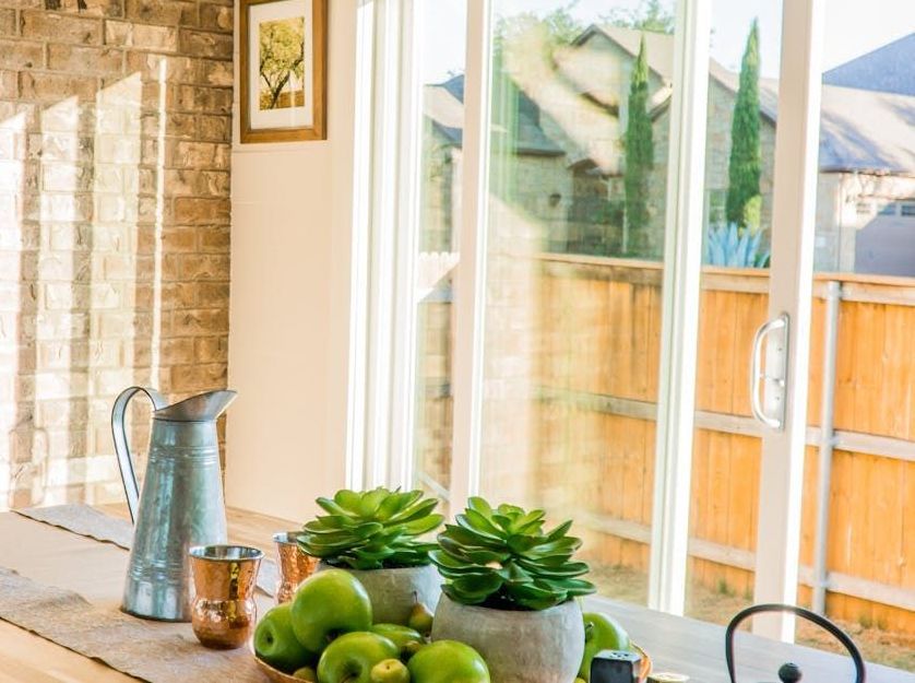 Table set with green apples, succulents, and a metal pitcher near a sliding glass door overlooking a backyard.