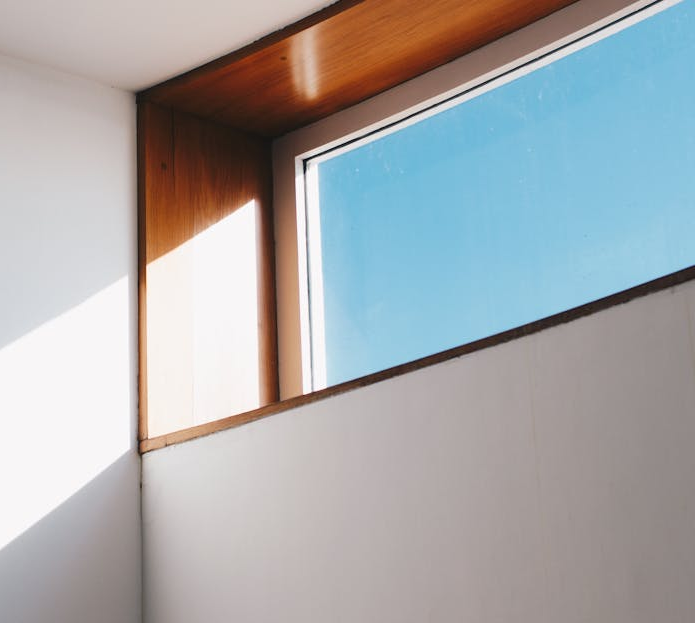 Brightly lit interior corner with a window showing a clear, blue sky. Wooden trim surrounds the window.