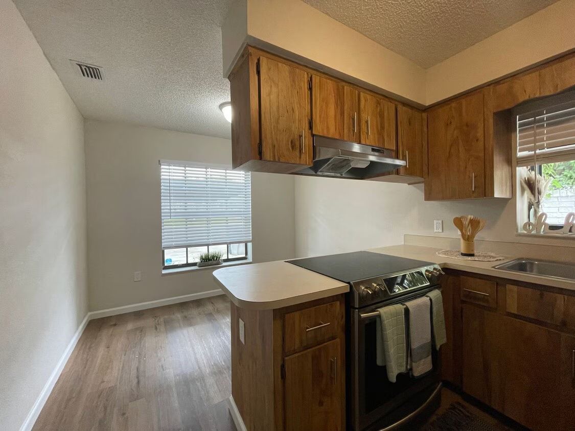 A kitchen with wooden cabinets , a stove , a sink , and a window.