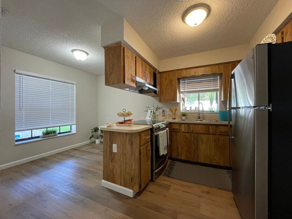 A kitchen with wooden cabinets , stainless steel appliances , a refrigerator and a window.