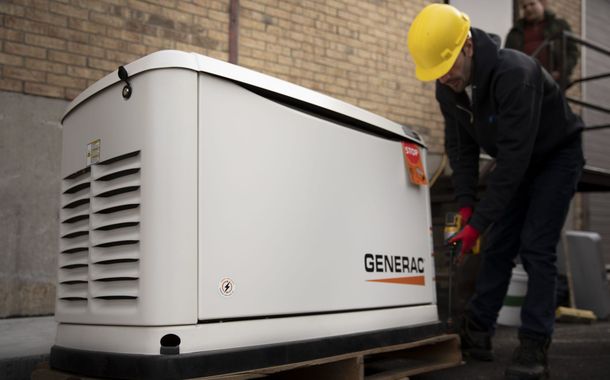 Un homme portant un casque jaune travaille sur un générateur Generac à l'extérieur.