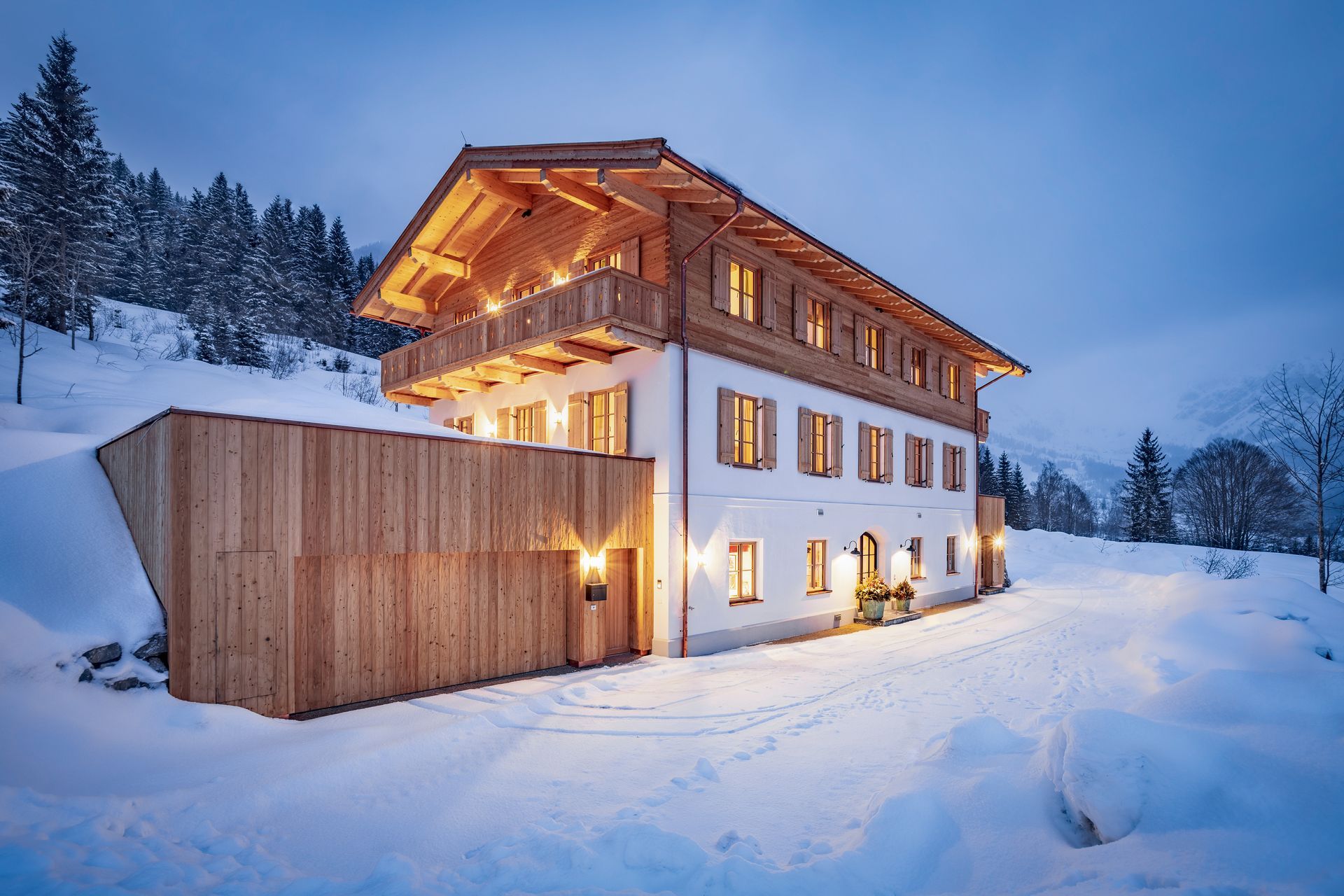Chalet enneigé avec des accents de bois, des fenêtres éclairées et un balcon sur fond de montagne.