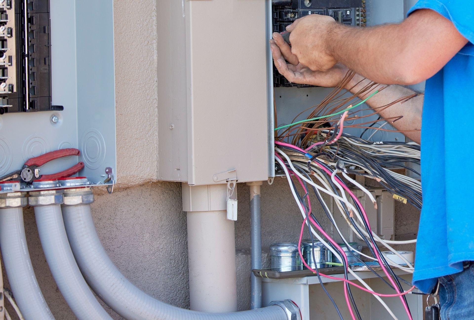 Électricien travaillant sur le câblage d'un coffret électrique extérieur. Les fils sont visibles, les mains tenant les connexions.