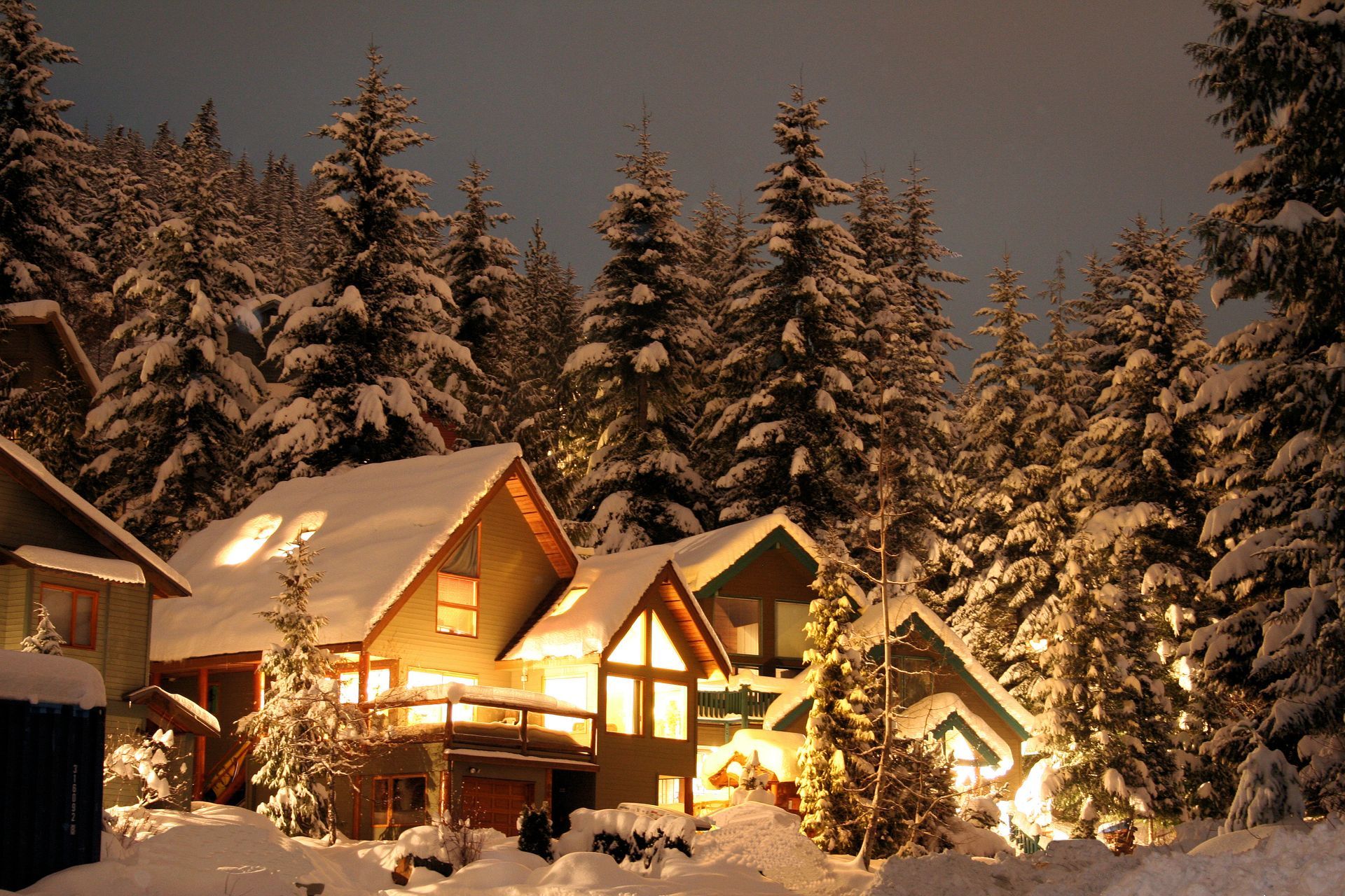 Snow-covered cabins nestled in a winter forest, lit with warm lights at night.
