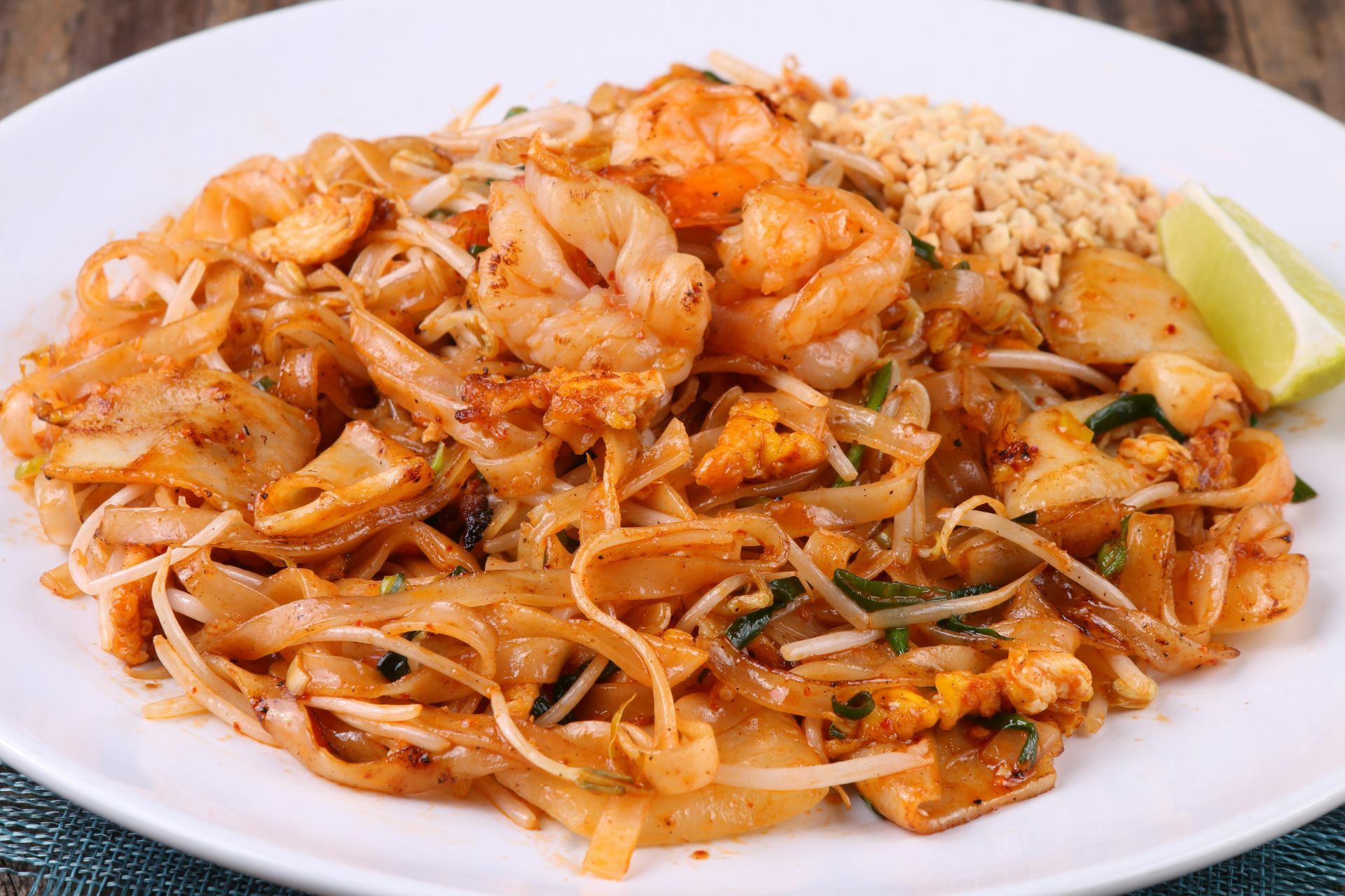 A plate of stir-fried Pad Thai noodles with shrimp, bean sprouts, crushed peanuts, and a lime wedge.