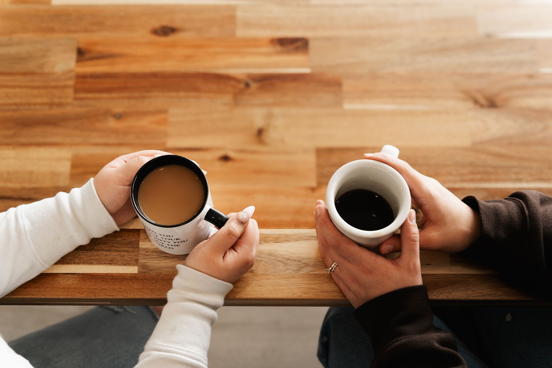 Two women hold coffee mugs with specialty roasted coffee at table, friendship and community around coffee