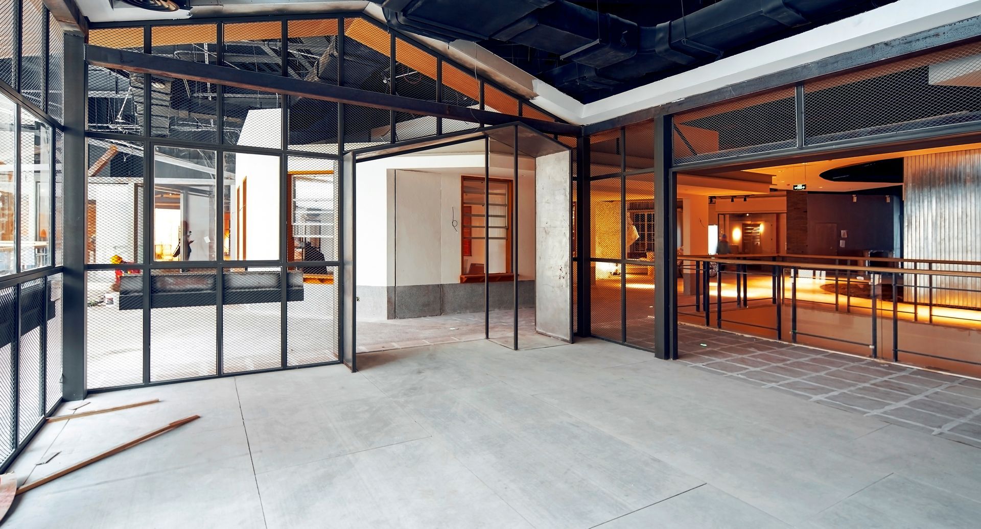 Empty industrial interior with exposed steel framing, concrete floor, and warm orange lighting on the right